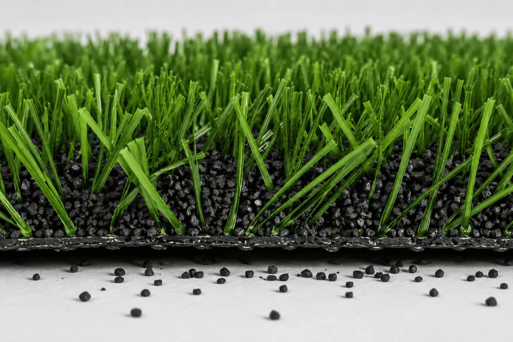 Cross-section of infilled sports turf showing black SBR rubber granules brushed between the fibres